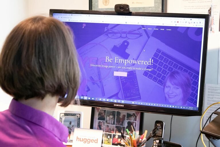 Woman in purple blouse viewing educational website on office computer monitor.